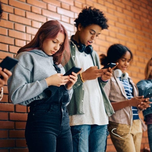 Multiracial group of teenagers using their cell phones at high school.